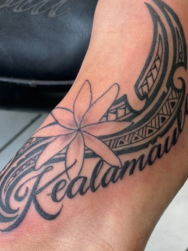 Polynesian foot tattoo by Benson Carlos with flower and script in Hawaii.